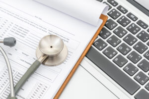 Virtual medical assistant tools for healthcare billing—clipboard with patient form, stethoscope, and laptop for digital documentation.