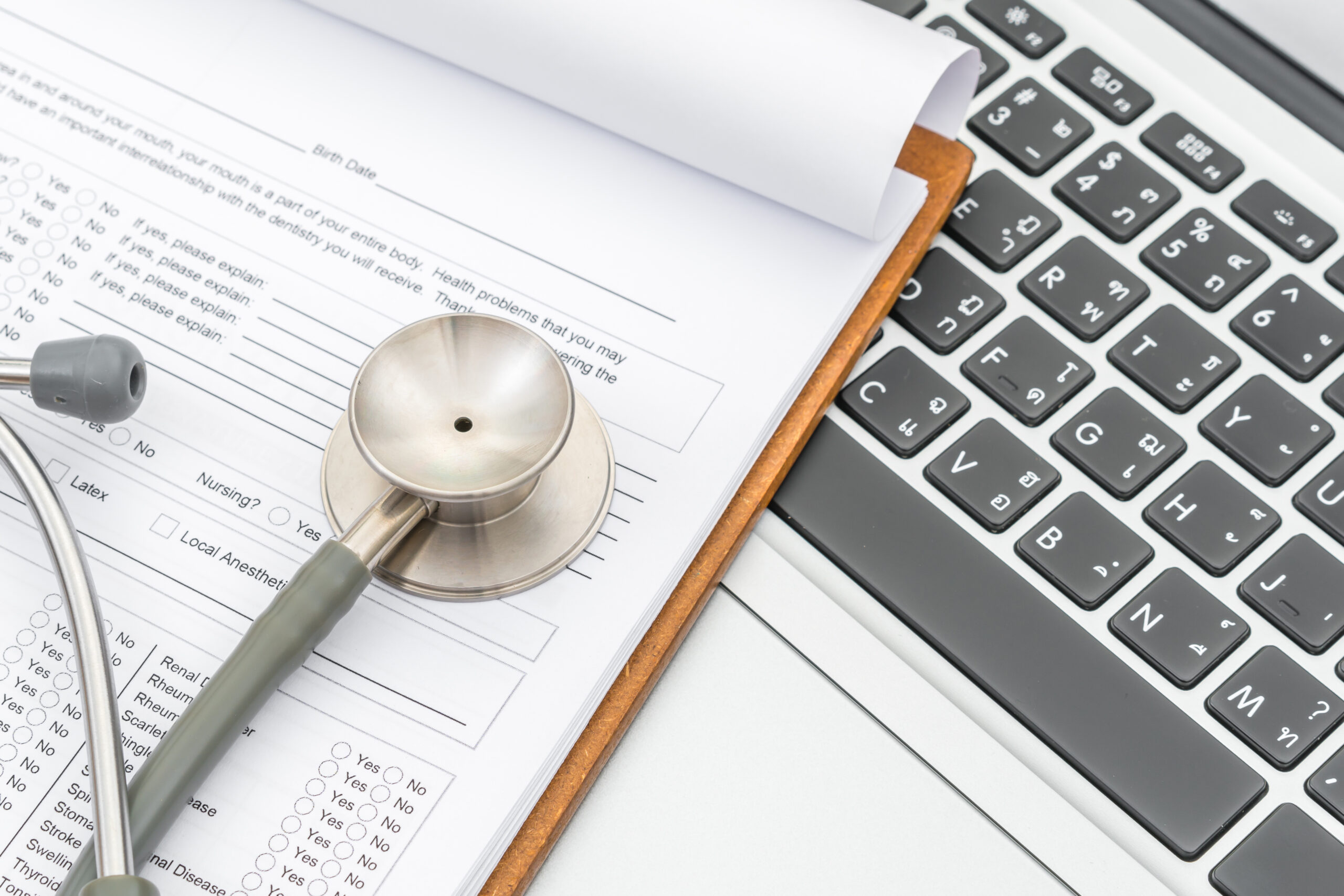 Virtual medical assistant tools for healthcare billing—clipboard with patient form, stethoscope, and laptop for digital documentation.